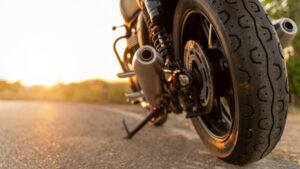 Motorcycle parked on an open road at sunset, with a close-up view of the rear tire, exhaust pipe, and suspension