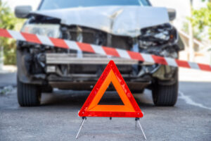 Red emergency stop triangle sign and Red warning police tape afore Destroyed car in car crash traffic accident on city road. Smashed broken car in accident.